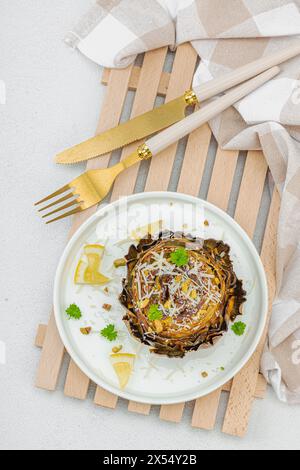 Köstliche gebackene Artischocke mit Parmesankäse und Pistazien. Olivenöl, Knoblauch, Petersilie und Zitrone. Weißer hölzerner Hintergrund, verzehrfertig vegane Speisen, Stockfoto