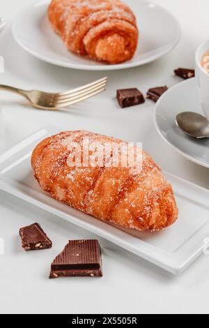 Nahaufnahme einiger xuixos de Crema, Gebäck gefüllt mit Vanillepudding typisch für katalonien, spanien, auf verschiedenen weißen Keramikplatten, neben einer Tasse Kaffee Stockfoto