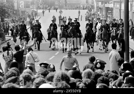 Für die Kameras spielen ein Demonstrator, der einem Fernsehteam beim Filmen im Weg steht. Lewisham London 1970s UK. Die berittene Polizei bewegt sich auf die Menge linker Demonstranten zu, die an der Front National protestieren und durch das neue Kreuz nach Lewisham marschieren. New Cross, London, England 13. August 1977. HOMER SYKES. Stockfoto