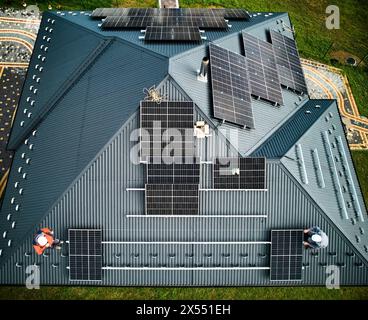 Blick von oben auf ein neues modernes Cottage mit PV-Solarpaneelen auf dem Dach. Installation von Solarbatterien durch zwei Fachkräfte. Moderne Ressourcen elektrischer Energie. Stockfoto