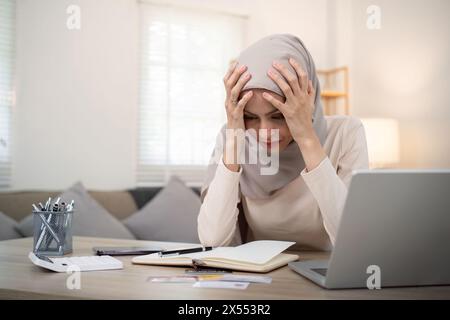 Muslimische Frau berechnet mit Rechner und Rechnungsbeleg unter Stress junge muslimische Frau, die Kopf bedeckt, hat sie finanzielle Probleme Stockfoto