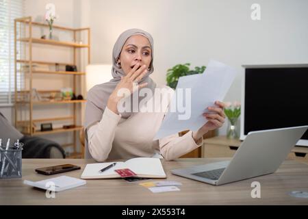 Junge beunruhigte und schockierte muslimische Frau im Hijab mit Dokumenten und Taschenrechner. Finanzielle Probleme mit Konten, Krediten, Familienhaushalt zu Hause Stockfoto