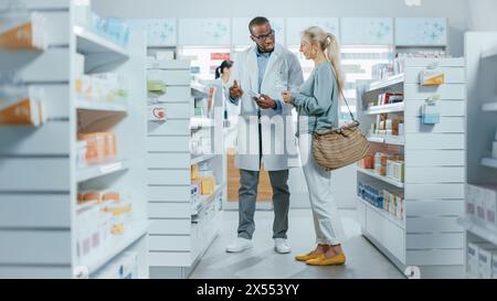 Apotheke: Professioneller schwarzer Apotheker, der kaukasischen Seniorinnen hilft, mit Medizin-Empfehlungen, Ratschlägen, Gesprächen. Cusotmer Unterstützung in Drogerie voll von Drogen, Pillen, Gesundheitsprodukten Stockfoto