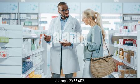 Apotheke: Professioneller schwarzer hilfreicher Apotheker, der kaukasische Senior weibliche Kundin mit Medikamentenempfehlung berät, spricht. Cusotmer Unterstützung in Drogerie voll von Drogen, Pille, Gesundheitsprodukte Stockfoto