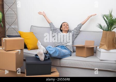 Junge Frau mit Lächeln sitzt bequem auf dem Sofa im Haus Stockfoto