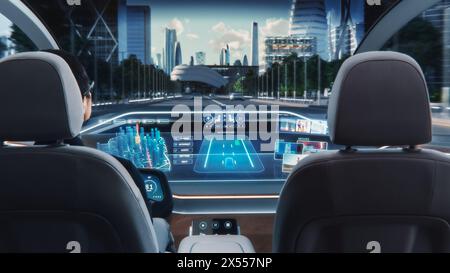 Futuristisches Konzept: Eleganter Geschäftsmann, der die Navigations-App auf einem Augmented Reality Dashboard mit Finanznachrichten nutzt, während er in einem autonomen, selbstfahrenden emissionsfreien Elektroauto sitzt. Stockfoto