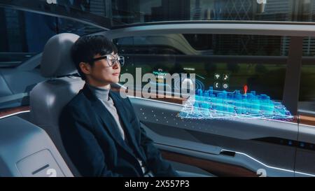 Futuristisches Konzept: Eleganter Geschäftsmann, der den Standort in einer interaktiven 3D-Navigations-App auf einem Augmented Reality Dashboard festlegt, während er in einem autonomen, emissionsfreien Elektroauto sitzt. Stockfoto