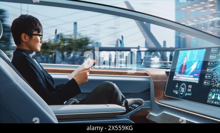 Futuristisches Konzept: Schöner, stilvoller japanischer Geschäftsmann in Brille, der Notizbuch liest und Nachrichten auf dem Augmented Reality Screen ansieht, während er in einem autonomen, selbstfahrenden emissionsfreien Auto sitzt. Stockfoto