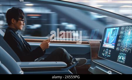 Futuristisches Konzept: Schöner, stilvoller japanischer Geschäftsmann in Brille, der Notizbuch liest und Nachrichten auf dem Augmented Reality Screen ansieht, während er in einem autonomen, selbstfahrenden emissionsfreien Auto sitzt. Stockfoto