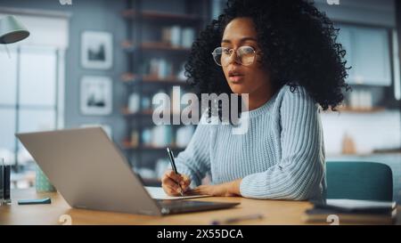 Wunderschöne authentische Latina-Frau, die an einem Schreibtisch in einem gemütlichen Wohnzimmer sitzt und an einer Videoschulstunde auf Laptop-Computer teilnimmt. Schüler Lernen Aus Der Ferne. Chatten Sie mit Freunden im sozialen Netzwerk. Stockfoto