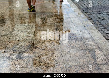 Reflexion auf dem nassen Boden durch den Regen von Fußgängern, die auf dem Gehweg vorbeifahren. Regnerischer Tag. Stockfoto