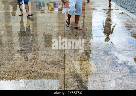 Reflexion auf dem nassen Boden durch den Regen von Fußgängern, die auf dem Gehweg vorbeifahren. Regnerischer Tag. Stockfoto