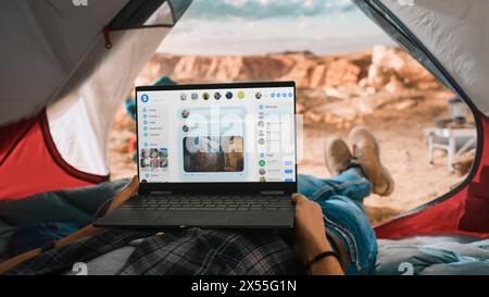 POV eines Touristen, der einen Laptop verwendet, um Social Network Feeds und die neuesten Fotos zu überprüfen. Reisender ruht in einem Zelt auf dem Rocky Mountain. Abenteuerlustiger Wanderer, der in der Natur lebt. Stockfoto