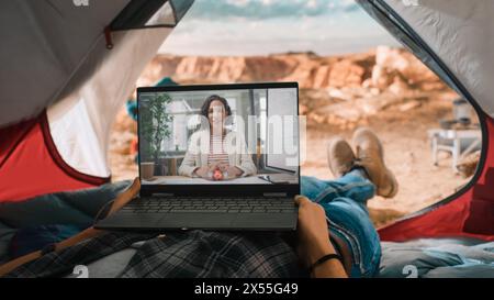 POV eines Touristen, der mit einem Freund oder Kollegen einen Videoanruf auf einem Laptop tätigt. Reisende, die sich in einem Zelt auf einem Rocky Mountain ausruhen. Abenteuerlicher Wanderer, der in der Natur lebt. Stockfoto