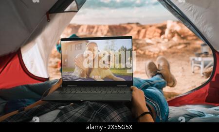 POV eines Touristen, der einen Videoanruf mit einem Freund macht, der mit Happy Dog auf einem Laptop spielt. Reisende, die sich in einem Zelt auf einem Rocky Mountain ausruhen. Abenteuerlicher Wanderer, der in der Natur lebt. Stockfoto