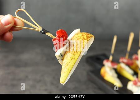 Frau mit leckerem Canape mit Birne, Blauschimmelkäse und Schinken am Tisch, Nahaufnahme Stockfoto