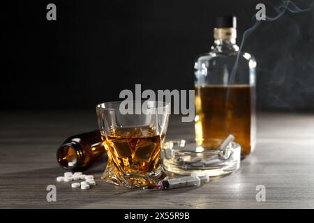 Alkohol- und Drogensucht. Whiskey in Glas, Spritze, Pillen und Zigaretten auf Holztisch Stockfoto