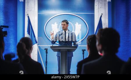 Junger Vertreter der Organisation beantwortet Fragen von Journalisten auf der Pressekonferenz. Pressesprecher, der beim Gipfeltreffen arbeitet. Minister im Gespräch mit dem Kongress. Hintergrund mit französischen Flaggen. Stockfoto