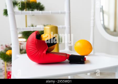 Sportausrüstung: Kurzhantel, Boxhandschuhe, Tannenzweig, Weihnachtsschmuck, Geschenke auf Stuhl. Stockfoto