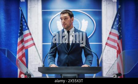 Junger Vertreter der Organisation beantwortet Fragen von Journalisten auf der Pressekonferenz. Pressesprecher, der beim Gipfeltreffen arbeitet. Minister im Gespräch mit dem Kongress. Hintergrund mit amerikanischen Flaggen. Stockfoto