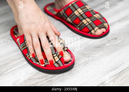 Ein Fuß in einen alten, undichten Slipper. Alter Pantoffel. Sneaker mit Lochmuster. Mann in alten Hausschuhen Stockfoto