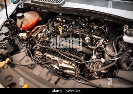 Von oben sichtbarer staubiger Pkw-Motor unter geöffneter Motorhaube mit verschiedenen montierten Ersatzteilen, während elektrische Kabel mit der Batterie und in Service s verbunden sind Stockfoto