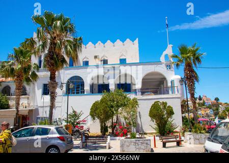 SYMI, Griechenland - 03. JUNI 2021: Das Gebäude der Polizeiwache befindet sich am Eingang zum Hafen von Symi neben dem Uhrturm (Roloi). Hel Stockfoto