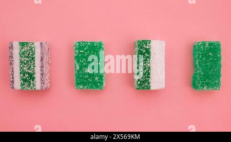 Vier quadratische Stücke gelatineartiger Süßigkeiten auf rosa Papierhintergrund. Flachlage von Marmeladenscheiben. Stockfoto