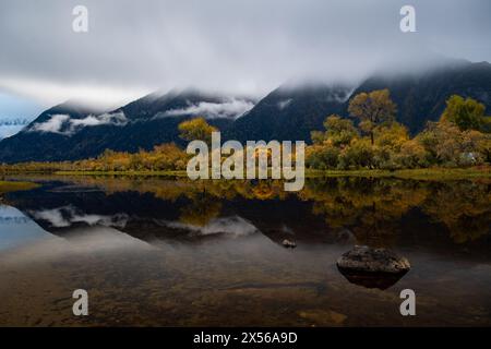 Goldene Ruhe: See umgeben von nebeligen Bergen, eingerahmt von den lebhaften Herbstbäumen. Stockfoto