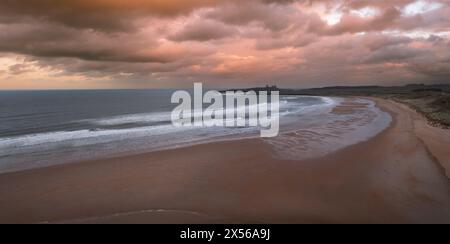 Panoramablick auf Sanddünen und Sandstrand in Embleton Bay und Dunstanburgh Castle am England Coast Path bei Sonnenuntergang Stockfoto
