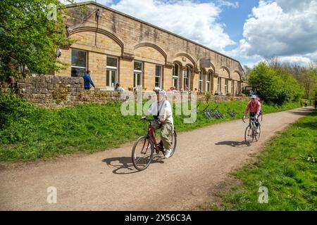 Die Leute radeln am Hassop Station Cafe vorbei, während sie entlang der stillgelegten Eisenbahnlinie des Monsal Dale Trail in der Nähe von Bakewell im English Peak District fahren Stockfoto