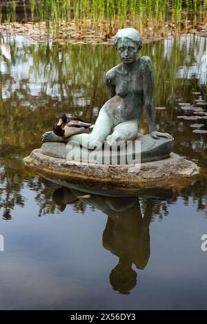 Statue eines sitzenden Mädchens, mit einer echten Ente an der Seite, im Wasser eines Teichs im Japanischen Garten, Margareteninsel Stockfoto