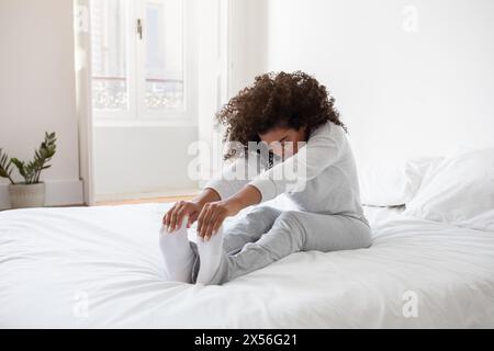Die junge Frau streckt ihre Beine auf einem Weißen Bett Stockfoto