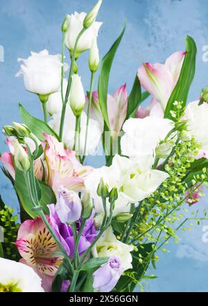 Eleganter Blumenstrauß mit weißem und lila Lisianthus, Alstroemeria und dekorativen Stielen Nahaufnahme auf blau strukturiertem Hintergrund Stockfoto