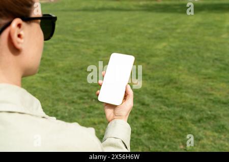 Mockup weißer leerer Bildschirm des Mobiltelefons in den Händen der Frau auf dem Hintergrund des grünen Rasens. Stockfoto
