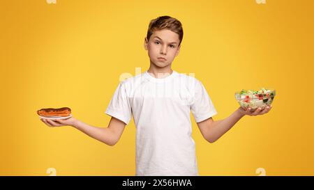 Trauriger Junge, der zwischen Gemüsesalat und Schokolade eclair wählt Stockfoto