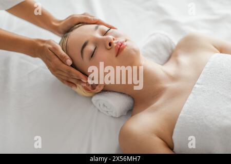 Ruhige junge Frau, die eine entspannende Kopfmassage genießt Stockfoto
