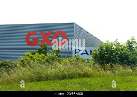 Lyon, Frankreich - 30. Mai 2023: Die Fassade eines GXO Logistiklagers, umgeben von üppigem Grün unter einem hellblauen Himmel. Stockfoto