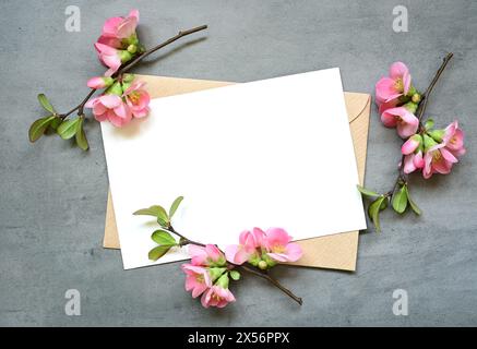 Leere weiße Grußkarte mit braunem Umschlag und roten Blumen auf grauem Hintergrund. Stockfoto