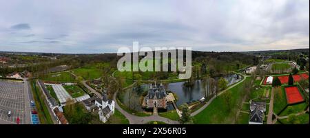 Huizingen, Belgien, 26. März 2024, dieses Panorama aus der Luft fängt die üppige, grüne Landschaft von Huizingen mit einem historischen Schloss an einem ruhigen See ein. Die weitläufigen Grünflächen, Erholungsbereiche wie Tennisplätze und gepflegt angeordnete Wege bieten einen ruhigen Rückzugsort in einer lebendigen natürlichen Umgebung, die durch die malerische Architektur und die weitläufige Aussicht der Stadt betont wird. Panoramablick auf die Landschaft von Huizingen mit historischem Schloss und umliegendem Park. Hochwertige Fotos Stockfoto