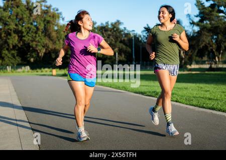 Weitwinkelansicht eines jungen Ehepaares, das an einem sonnigen Nachmittag im Sommer im Park läuft und seine Vitalität genießt. Stockfoto