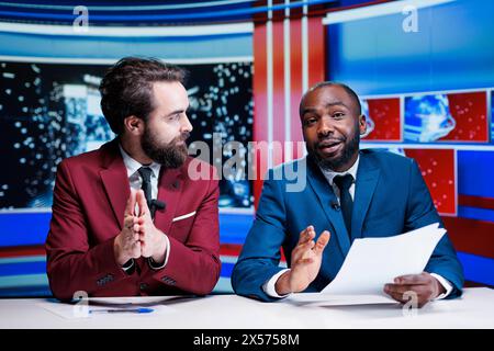 Das Reporter-Team präsentiert Nachrichtensegmente in einem Fernsehstudio, um eine Late-Night-Show zu veranstalten, in der wichtige globale Ereignisse angesprochen werden. Diverse Nachrichtensprecher übersenden Live-Reportagen, internationale Berichte. Stockfoto