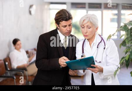 Aufmerksame leitende Ärztin verschreibt Tests an Patienten der Klinik, um den Gesundheitszustand zu überprüfen Stockfoto