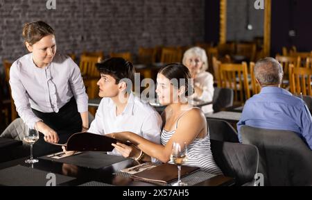 Die Kellnerin nimmt die Bestellung von einem jungen Paar im Restaurant entgegen Stockfoto