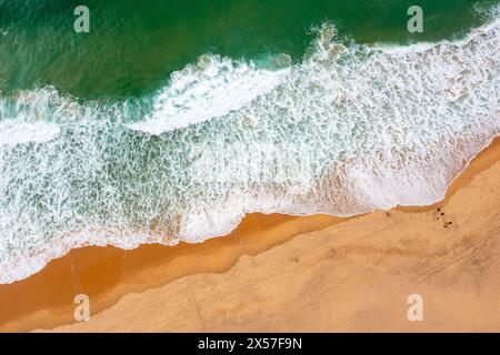 Drohnenansicht mit wunderschönen, nahtlosen Aufnahmen, während türkisfarbene Wellen an der sandigen Küste aufbrechen. Luftaufnahme des goldenen Strandes, der tiefes blaues Ozeanwasser und schaumige Wellen trifft Stockfoto