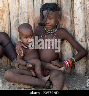 Himba-Mädchen mit geflochtenen Flechten mit Baby, in der Nähe von Opuwo, Kaokoveld, Kunene, Namibia Stockfoto