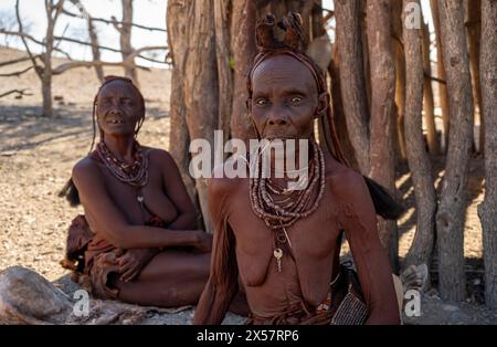 Eine alte Frau aus Himba mit traditionellem Kopfschmuck vor einer Hütte in der Nähe von Opuwo, Kaokoveld, Kunene, Namibia Stockfoto