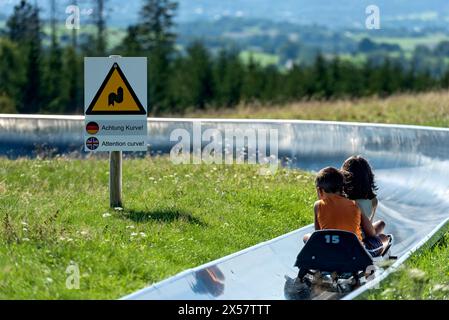 Junge und Mädchen mit Schlitten auf der Sommerrodelbahn, Warnschild Aufmerksamkeitskurve, Ski- und Rodelarena, Gipfelberg Hoherodskopf, Ausflug Stockfoto