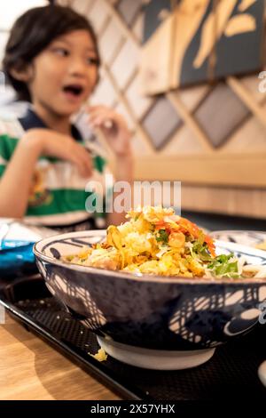 Eine Schüssel Nudelmenü im japanischen Restaurant mit einem glücklichen kleinen asiatischen Jungen im Hintergrund Stockfoto