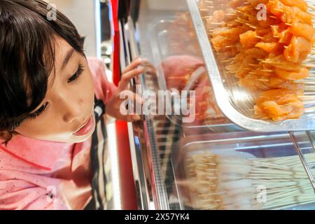 Südostasiatische Jungen zeigen Interesse an Snacks, die an einem lokalen Satay-Stand ausgestellt werden Stockfoto